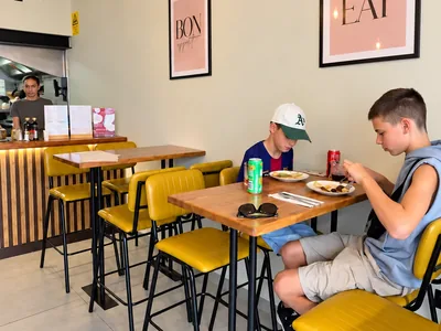 Interior acolhedor do Bom Crepe, com plantas suspensas, mesas de madeira e cadeiras amarelas