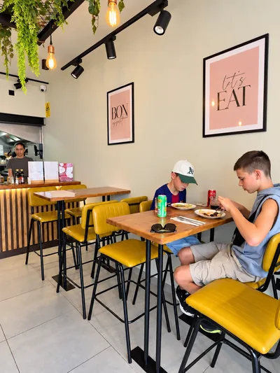 Mesas de madeira e cadeiras amarelas no interior do Bom Crepe Bistro