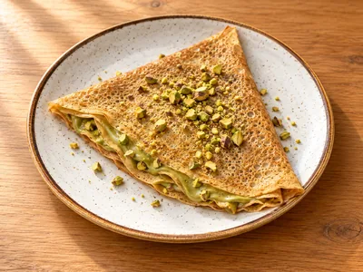 Crepe fino com creme de pistáchio e pistáchios sobre um prato de cerâmica