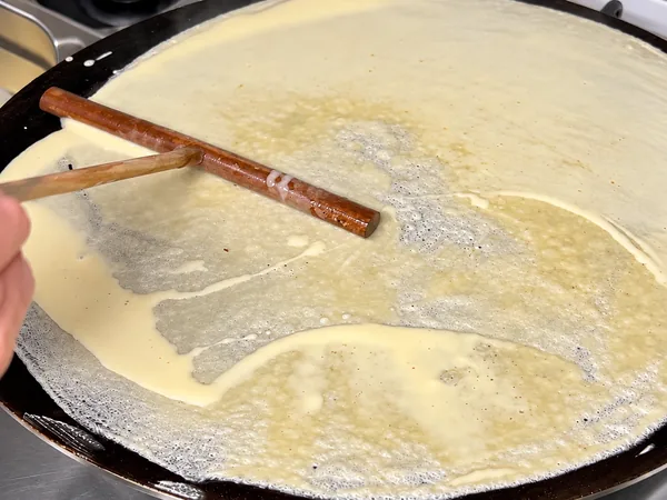 A massa fina de um crepe a ser espalhada na chapa com um utensílio de madeira